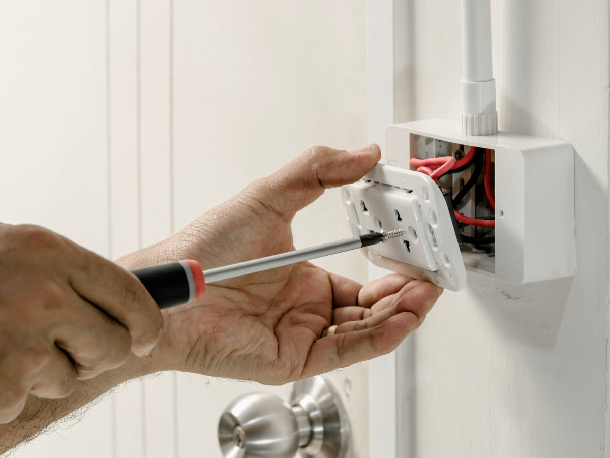 Person using a screwdriver to install or adjust an electrical outlet.