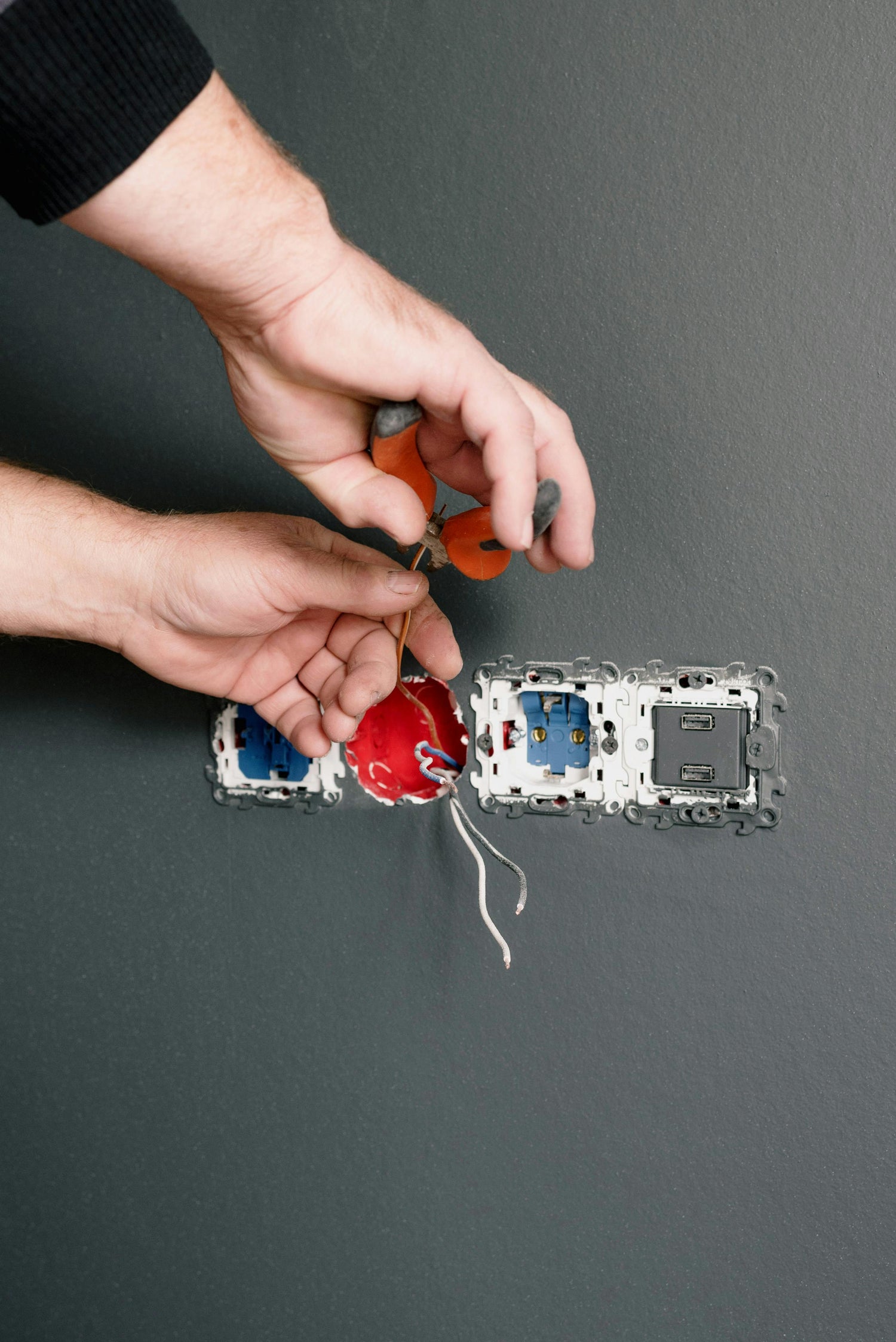 Person installing electrical wiring on a wall switch against a gray background